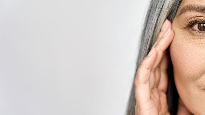 Beautiful older woman with grey hair touching her cheekbone